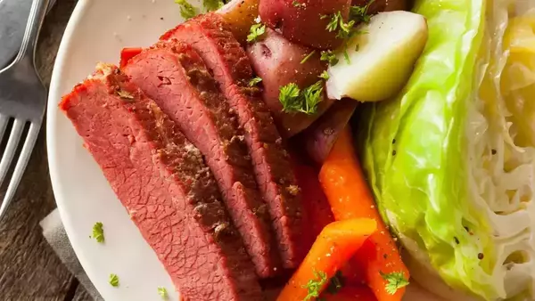 Close up view of corned beef, cabbage, carrots, and potatoes on a white plate with a silver spoon to the left.