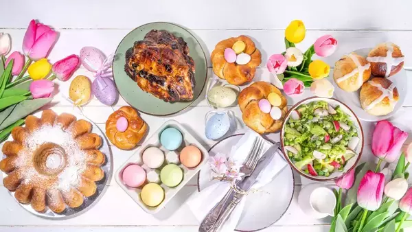 A lineup of Easter Brunch foods, surrounded by colorful Easter eggs and multi-colored tulips. All items sit on a white wood background.