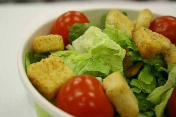 Close up view of a bowl of salad including items like iceberg lettuce, red tomatoes, and croutons.