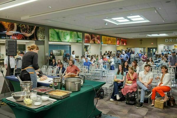 Chef Abra Berens cooks a meal on stage while an audience of students, staff, and faculty watch in rows of silver seats in North Dining Hall.
