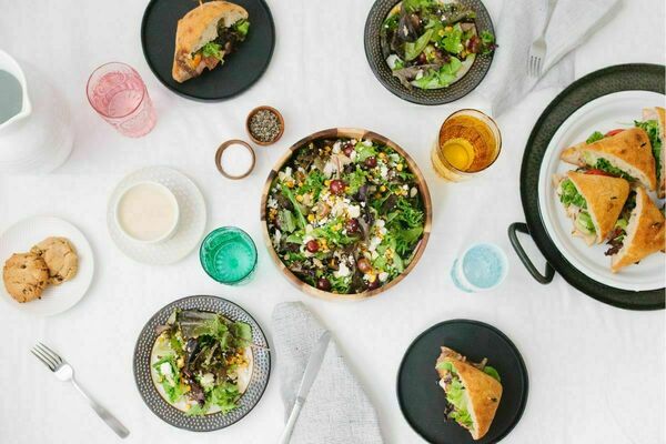 Top-down view of Modern Market dishes like salad and sandwiches. The dishes are posed next to multi-colored drinking glasses and sauces.
